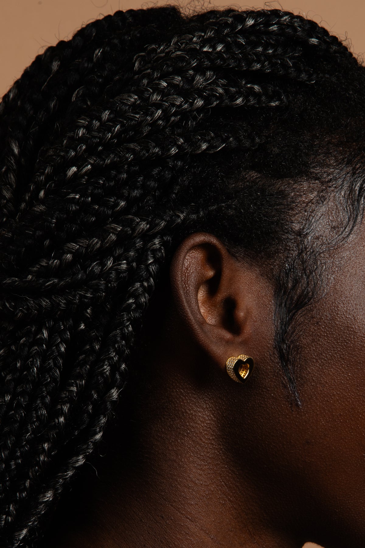 A close-up profile featuring the CASA London Akoma stud earring. The heart-shaped gold piece features a sophisticated hollow center and a pavé-set border of small, clear stones, showcasing a blend of traditional symbolism and modern luxury.