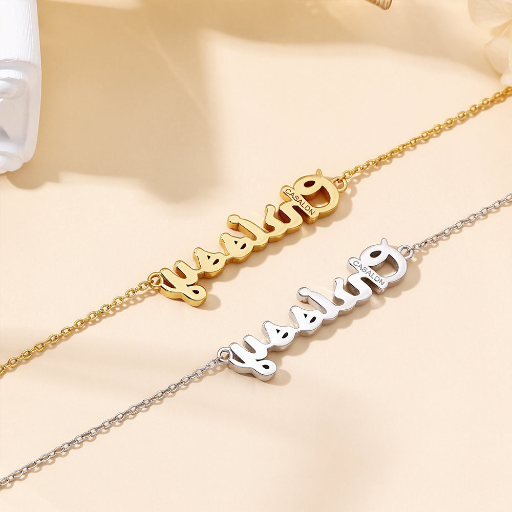 Flat lay of two CASA London Custom Pavé Name Necklaces side by side on a cream background, one in 18ct gold vermeil and one in rhodium silver on S925 sterling silver, both displaying the engraved CASA London brand insignia on the pendant.