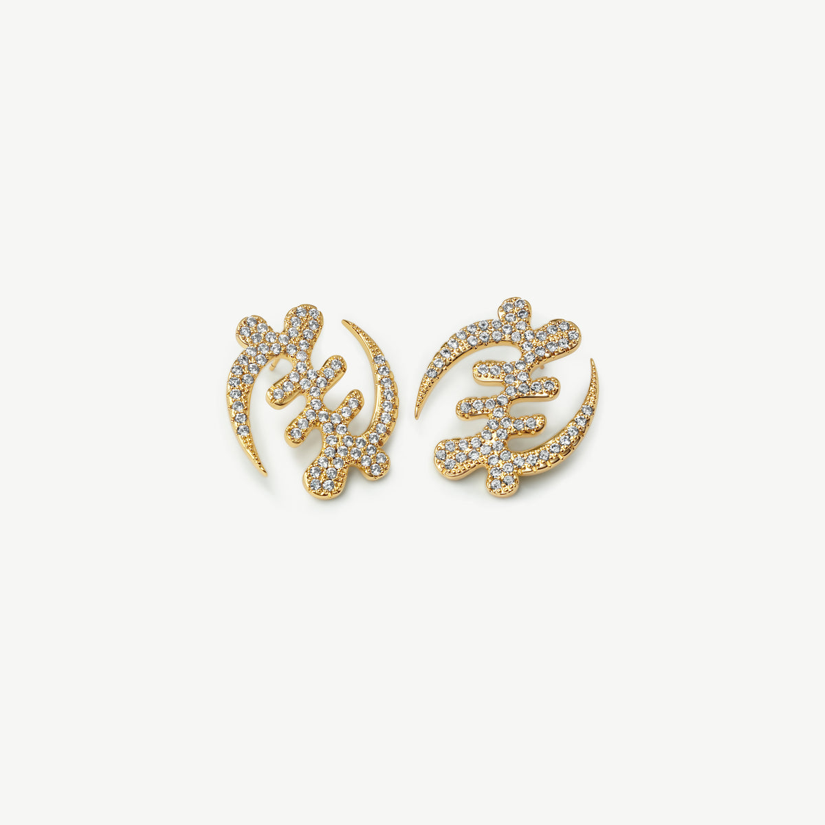 A high-resolution product shot of CASA London's 18k gold plated Gye Nyame Pavé oversized statement Earrings. The pair is shaped into the iconic Adinkra symbol, signifying the supremacy of God, and is intricately encrusted with shimmering pavé-set stones. Set against a minimalist white background, the design highlights the brand’s signature blend of cultural heritage and sophisticated modern luxury.