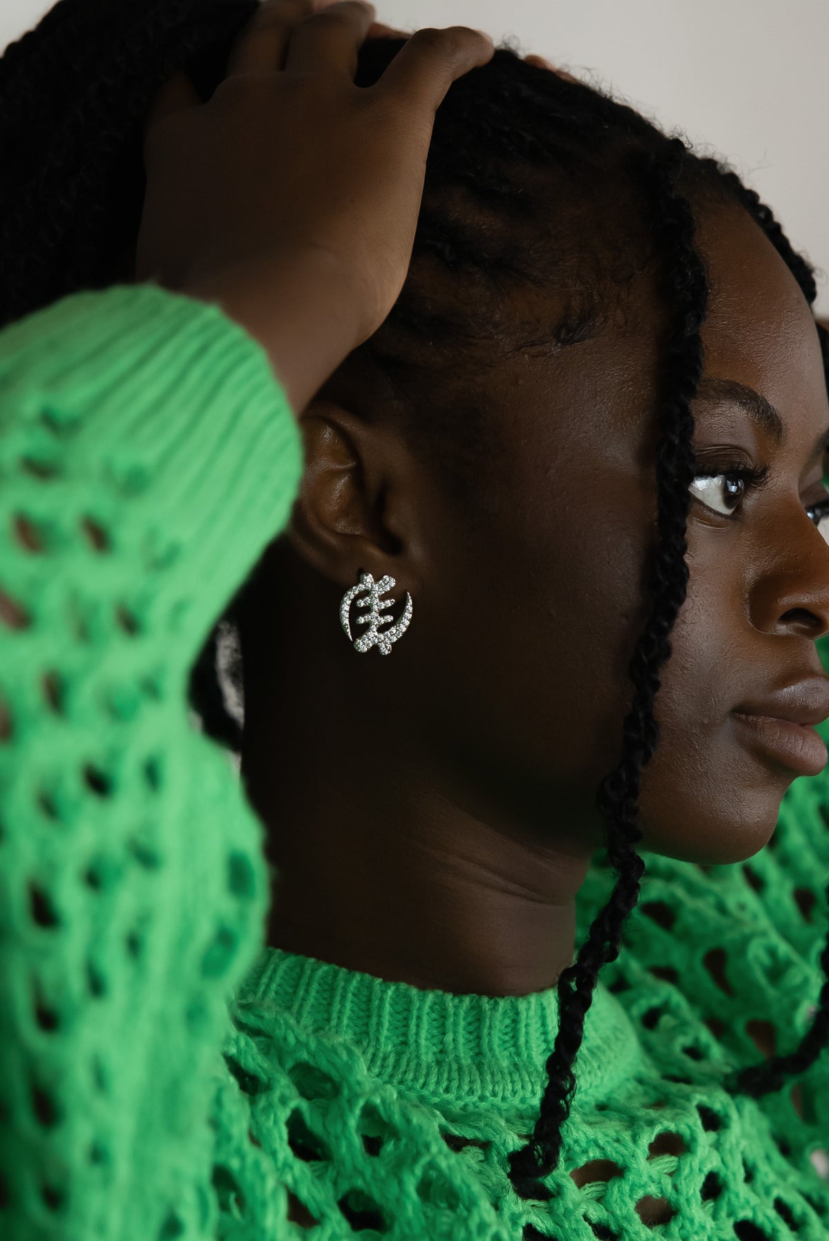 Woman with braided hair wearing silverGye Nyame Adinkra symbol stud earrings with pavé-set high-grade zircon stones. Model is looking from the side.