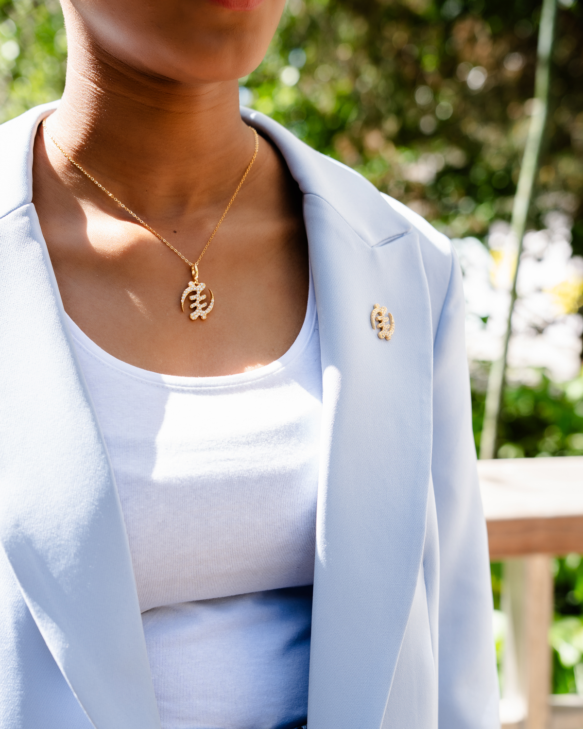 CASA LONDON Gye Nyame Pendant in 18ct gold plated, worn by a model. Symbolizing the 'Supremacy of God', this pendant also adds cultural significance to your look, versatile and timeless, pair it with a chain or bracelet for a complete look.