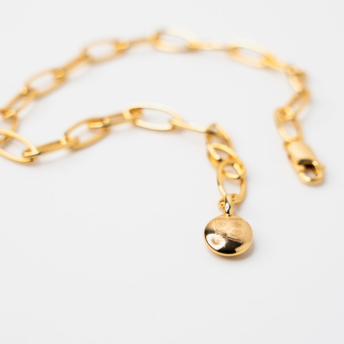 Gold vermeil link chain bracelet featuring a polished oval charm engraved with CASA London logomark engraved in tag, displayed on a clean white background.